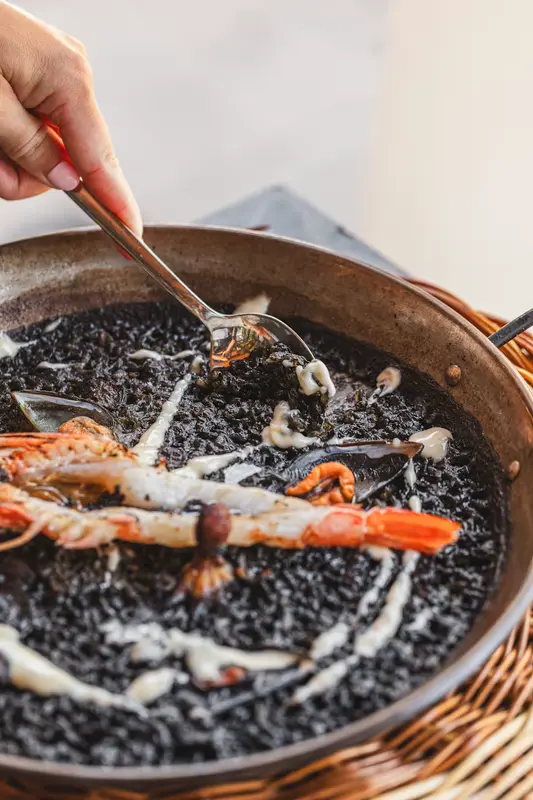 Arroz negro en paella individual con “allioli negat” y gambitas arroceras